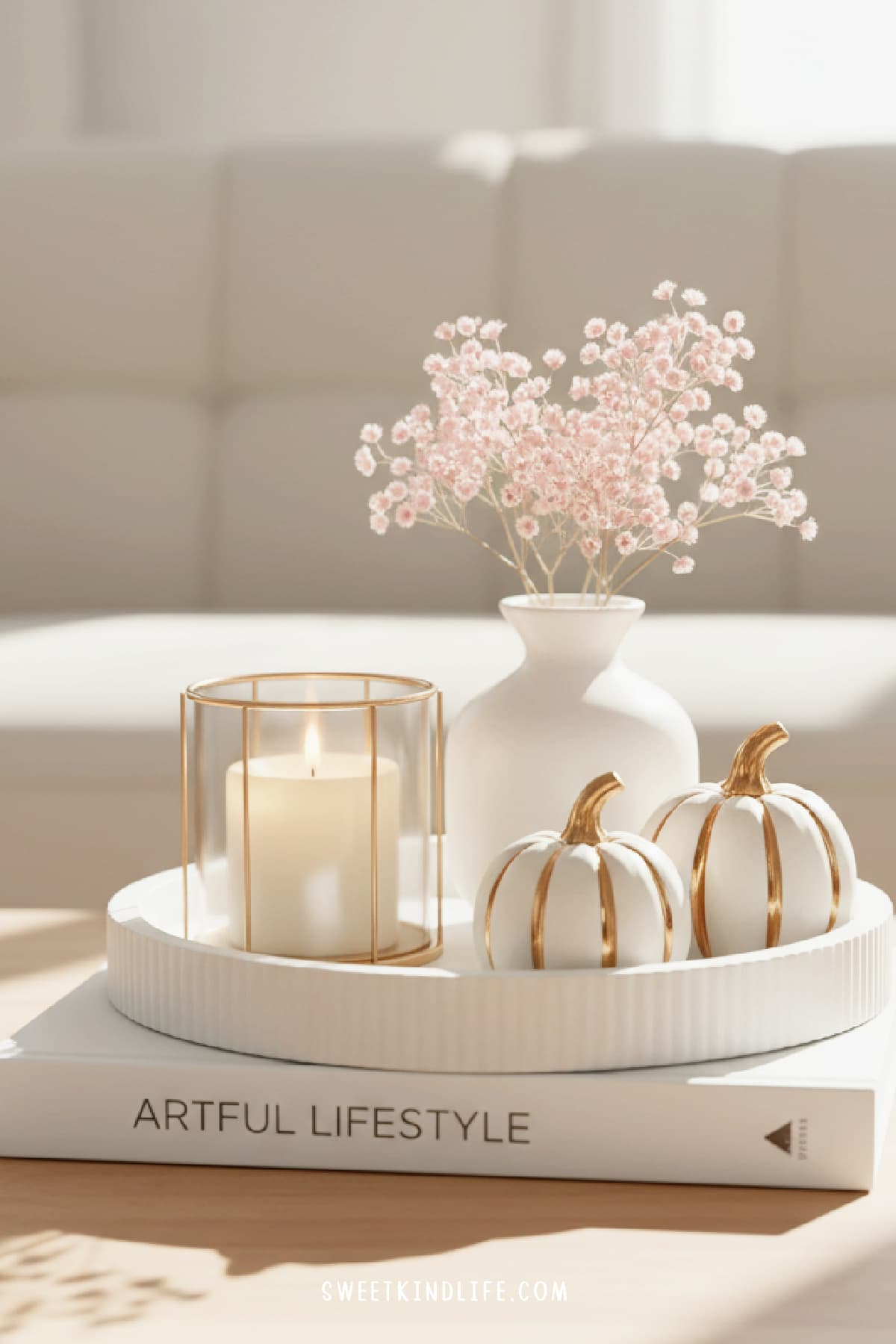 a photo of a living room with fall coffee table decor of a faux book with a white concrete tray on top and decorative pumpkins, candle and vase with pink flowers are on top